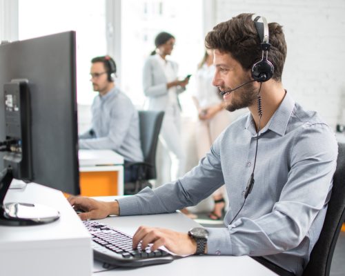 Smiling handsome customer support operator agent with hands-free device working in call center